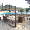 Espace détente avec voile d’ombrage tendue sur poteaux bois, terrasse bois et salon extérieur au bord d’une piscine.