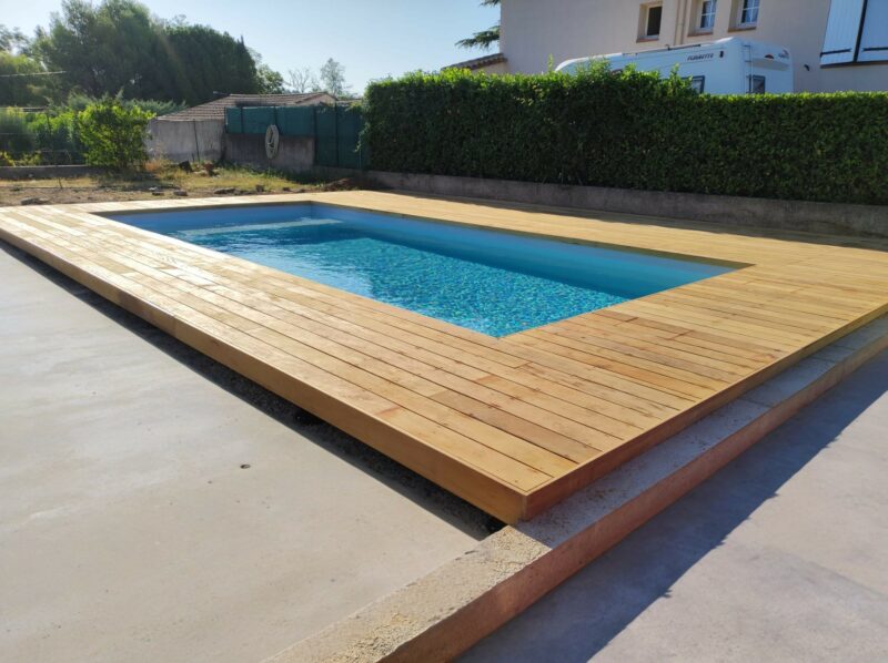 Terrasse en bois exotique Garapa entourant une piscine rectangulaire, avec une teinte jaune clair naturelle et une finition lisse, située à Béziers.