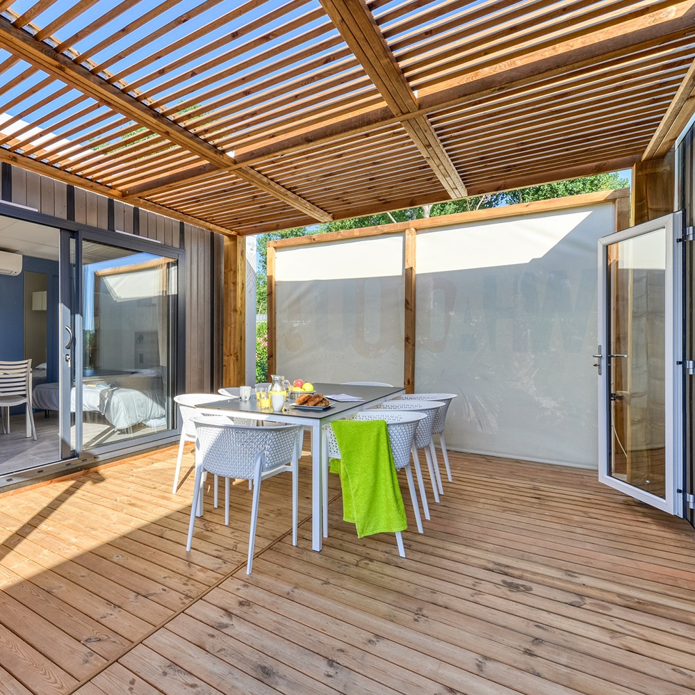 Pergola Éole bois avec toiture claustra et brise-vue textile gris sur terrasse mobile home avec salon de jardin