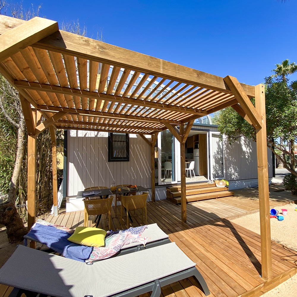 Pergola Éole bois grand format avec toiture claustra fixe sur terrasse de mobile home avec transats