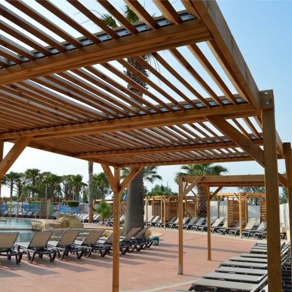 Installation de plusieurs pergolas Éole bois grand format autour d'une piscine de camping avec transats