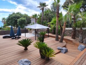 Terrasse en Itauba réalisée par Occia, avec palmiers et aménagement paysager en bord de mer.